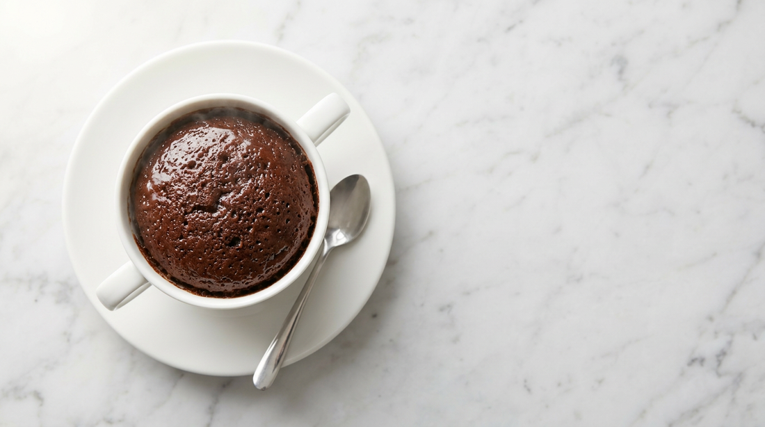 high-protein mug cake recipe in a white mug on a plate with a spoon on marble surface.