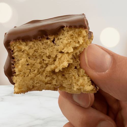 Hand holding a piece of Vanilla Protein Cake Mix topped with chocolate, showcasing a healthy dessert option.